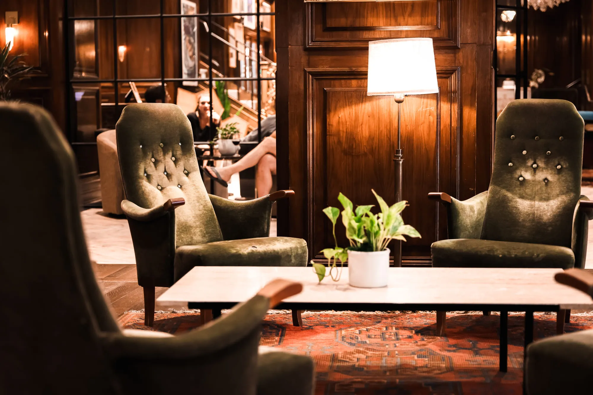 Green velvet armchairs around a low table with a potted plant in a wood-panelled lounge
